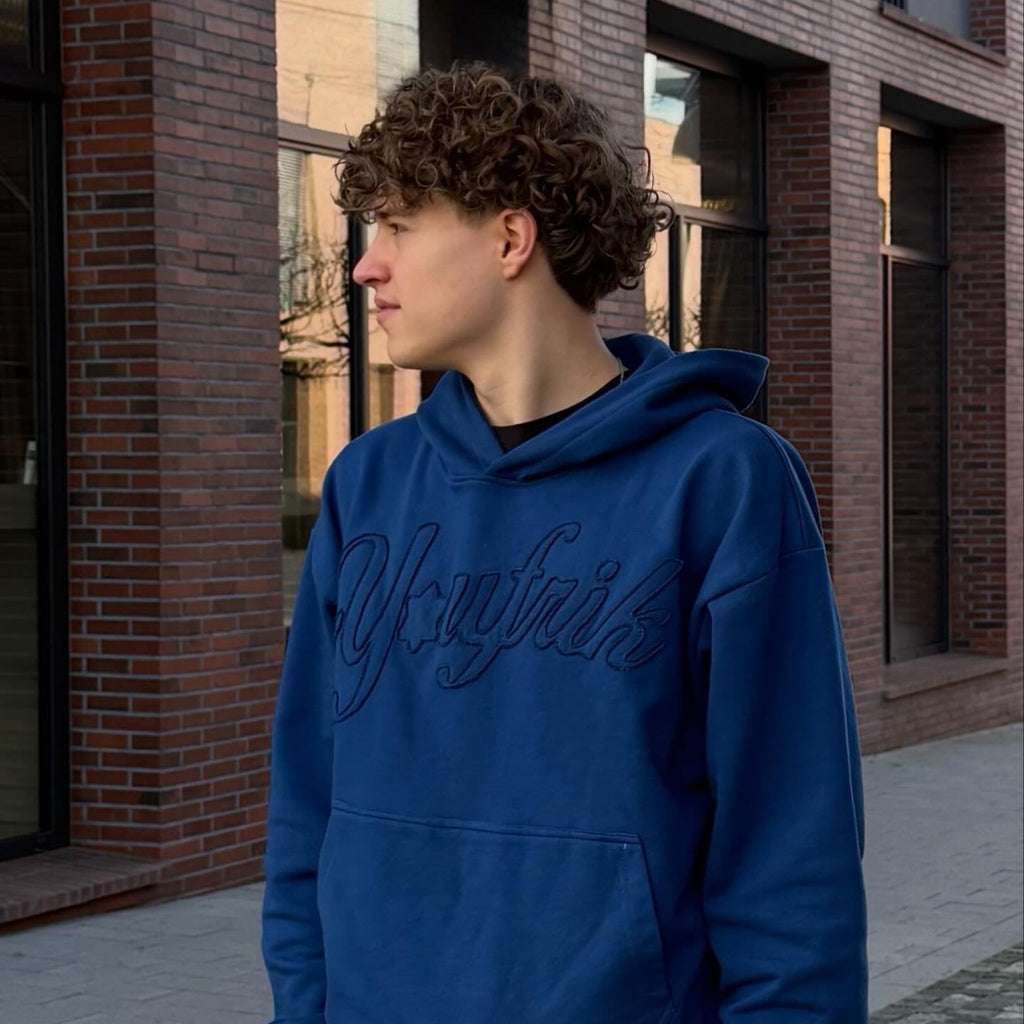 Junge steht mit blauen Pullover vor einer gemauerten Wand