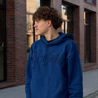 Junge steht mit blauen Pullover vor einer gemauerten Wand