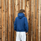 Junge mit blauem Hoodie vor einer Holzwand