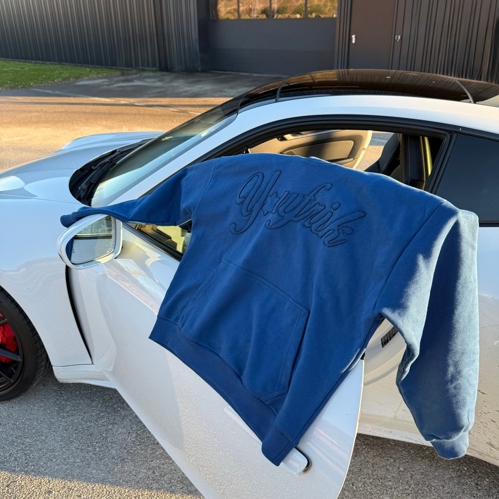 Blauer Pullover hängt über der Autotüre eines weißen Autos