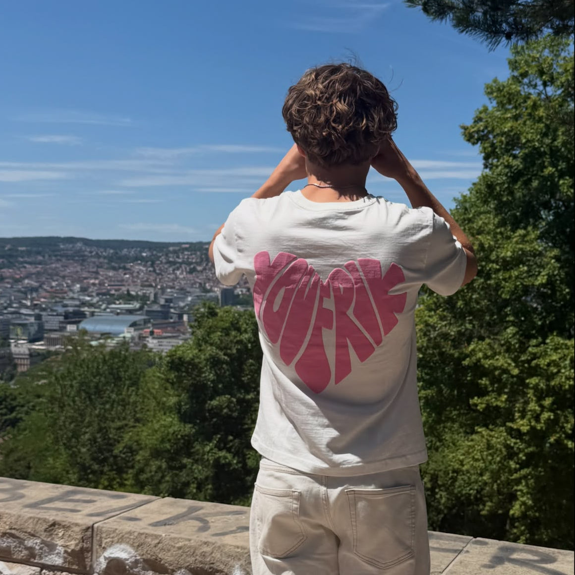 weißes T-Shirt mit pinkem herz Backprint wird von einem Mann getragen, der über eine Stadt blickt. 